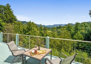 Un balcon avec une table dressée pour un repas, donnant sur un paysage boisé.