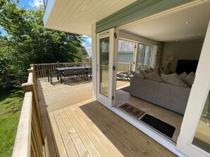 Une terrasse avec une table et des chaises, une porte-fenêtre coulissante donnant sur un espace de vie comprenant un canapé et une lampe.