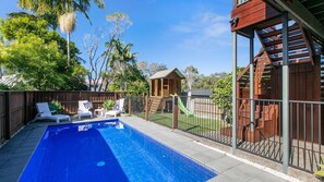 A backyard with a swimming pool, a wooden playhouse, and a slide.