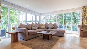 Ein geräumiges Wohnzimmer mit einer großen Eckcouch, einem Couchtisch und einem Korbstuhl.