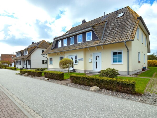 A two-story residential building with a tiled roof, a small front garden, and a paved driveway. - Ground floor apartment - house south beach (Mönchgut)