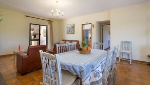 Ein Essbereich mit einem Tisch, gedeckt für vier Personen, umgeben von weißen Stühlen, einem braunen Sofa und einer Chandelier.
