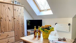 Ein Zimmer mit einem Holzkabinett, einem Tisch mit einer Zeitschrift, zwei Flaschen und einem Blumenstrauß.
