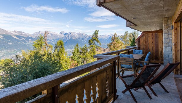 Ein hölzerner Balkon mit Blick auf Berge, eine Steinmauer und Gartenmöbel.