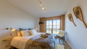 Ein Schlafzimmer mit einem großen Bett, einem Holzkopfteil, zwei an der Wand befestigten Stand-Up-Paddles, einem Sessel und einem Fenster mit Blick auf die Berge.