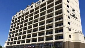Un hotel de varios pisos con una cuadrícula de balcones, un letrero llamativo en la esquina y un cielo azul despejado al fondo.