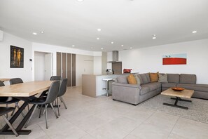 Una sala de estar moderna con un sofá gris, una mesa de comedor con sillas y una zona de cocina con un electrodoméstico rojo.