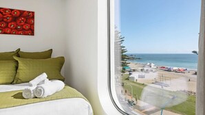 A hotel room with a bed, green pillows, a painting of red peppers, and a view of a beach with tents and umbrellas. - Oceanside Bliss Absolute Beachfront Stunning Views (Mount Maunganui)
