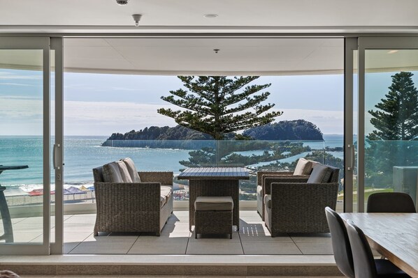 Un balcone con mobili in vimini, una porta vetrata e vista sul mare e un'isola in lontananza.