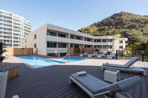 A hotel with a swimming pool, lounge chairs, and a view of a mountain. - Breakwater - Views, Pool, Sauna and Gym (Mount Maunganui)