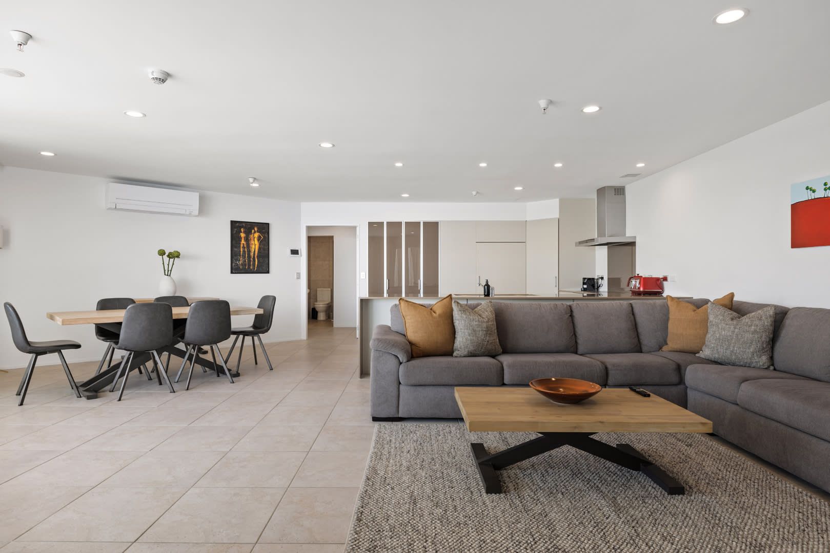 Un salon moderne avec un canapé gris, une table basse en bois et un coin repas comprenant une table et des chaises.