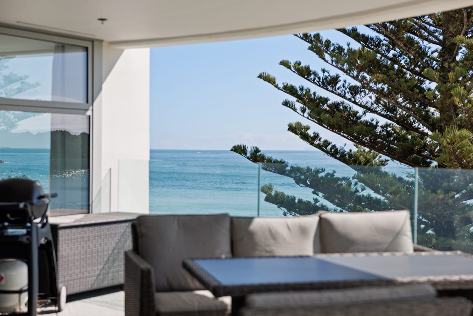 A modern outdoor seating area with a view of the ocean and a pine tree.