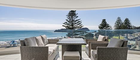 A covered outdoor seating area with wicker furniture and a view of the ocean.