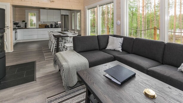 Ein modernes Interieur mit einem dunkelgrauen Sofa, einem Holztisch und einem Essbereich mit weißen Stühlen.