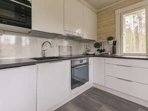 Une cuisine moderne avec des armoires blanches, un four en acier inoxydable, un comptoir noir et une fenêtre donnant sur les arbres.