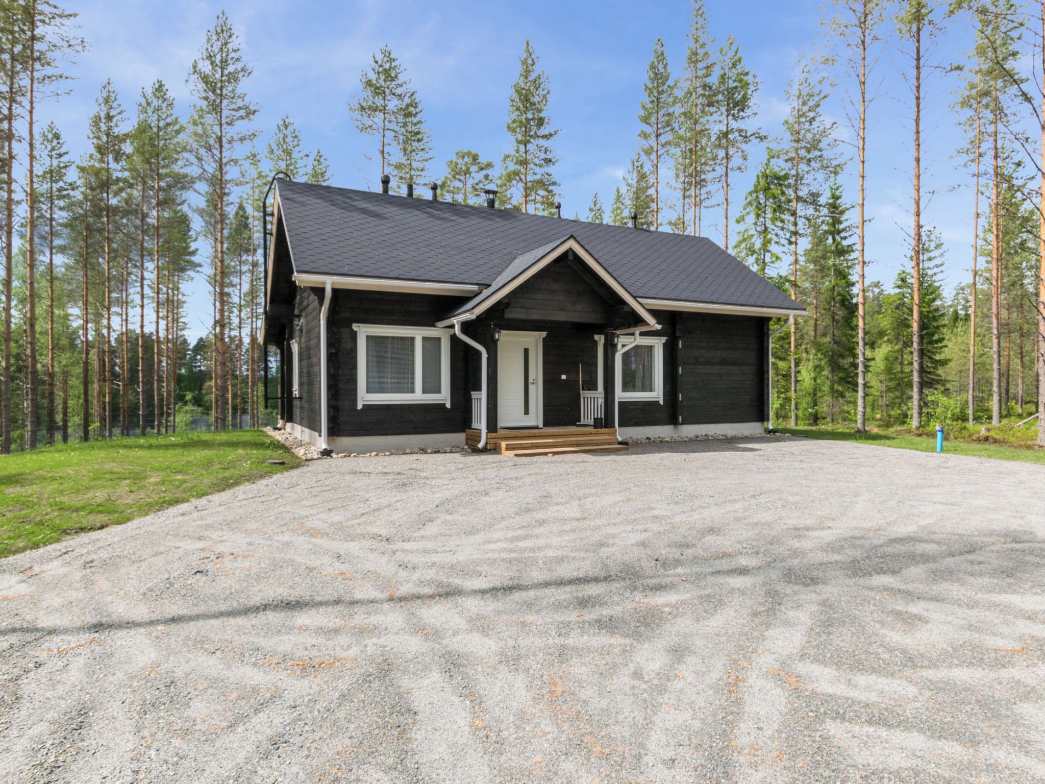 A two-story cabin with a gravel driveway, surrounded by a forest.