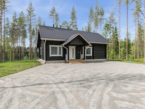 Une cabane à deux étages, avec une allée en gravier, entourée d’une forêt.