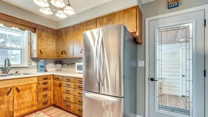 A kitchen with wooden cabinets, a stainless steel refrigerator, a window, and a door with a frosted glass panel. - Eagle River Lakefront Oasis w/ Private Dock! (Eagle River)
