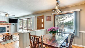 A spacious dining area with a wooden table and chairs, a fireplace, and a large window overlooking a lake. - Eagle River Lakefront Oasis w/ Private Dock! (Eagle River)