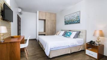 Una habitación de hotel moderna con cama, escritorio, silla, mesita de noche con lámpara y televisor montado en la pared.