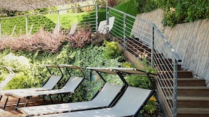 Une terrasse avec des chaises longues, un escalier en bois et une rambarde en métal.