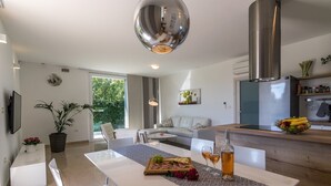 A modern kitchen with a central island, a dining area with white furniture, and a large window providing a view of greenery outside. - Beautiful villa with private pool, 3 bedrooms, 3 bathrooms, near the seaside! (Fazana)