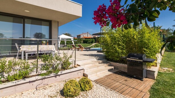 A modern outdoor patio with a barbecue grill, seating area, and a view of a swimming pool. - Beautiful villa with private pool, 3 bedrooms, 3 bathrooms, near the seaside! (Fazana)