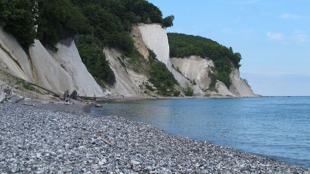 Une plage rocheuse, bordée de falaises, sous un ciel dégagé.