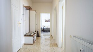Un couloir avec des portes blanches, un banc doté d’un coussin à motifs et un radiateur sur le côté droit.