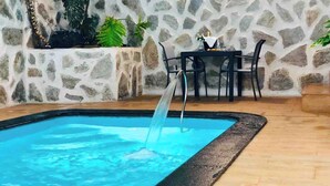 A swimming pool with a water feature, surrounded by stone walls and potted plants. - Canaryislandshost l Nazaret Suites (Nazaret)