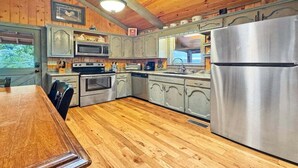 A kitchen with wooden cabinets, a stainless steel refrigerator, and a wooden dining table. - A Beary Nice View- Pet Friendly | Screened Porch | My Mountain | No steps to enter (Morganton)