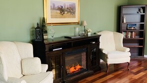 A living room with a fireplace, two white armchairs, a bookshelf, and a framed picture on the wall. - Raven Fox Farm-Country Charm! 5 BR Only 8 miles from Keeneland and BG Airport (Versailles)