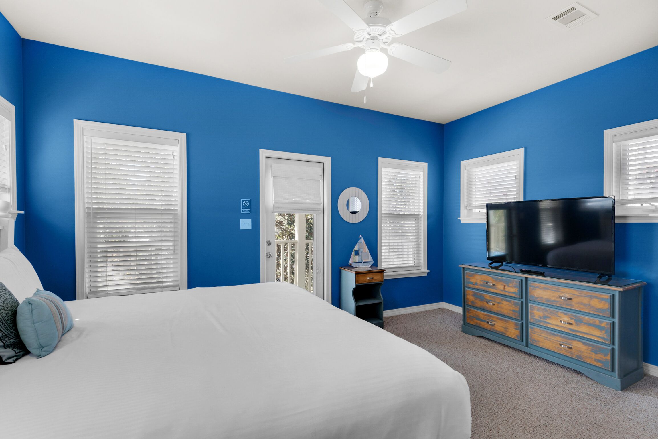 A bedroom with a large bed, a dresser, a television, and a ceiling fan.