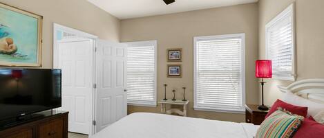 A bedroom with a bed, a ceiling fan, a TV, white walls, and a door.