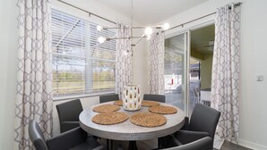 Un coin repas comprenant une table ronde, six chaises, un vase décoratif placé au centre et des rideaux à motifs.