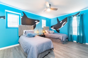 A room with two beds, a ceiling fan, and a large wall mural of orcas.