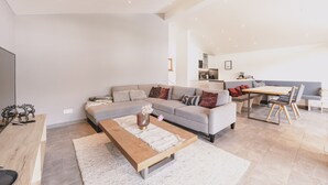 A modern living room with a sofa, coffee table, and a dining area with a table and chairs. - First IN Mountain Chalet A (Kaprun)