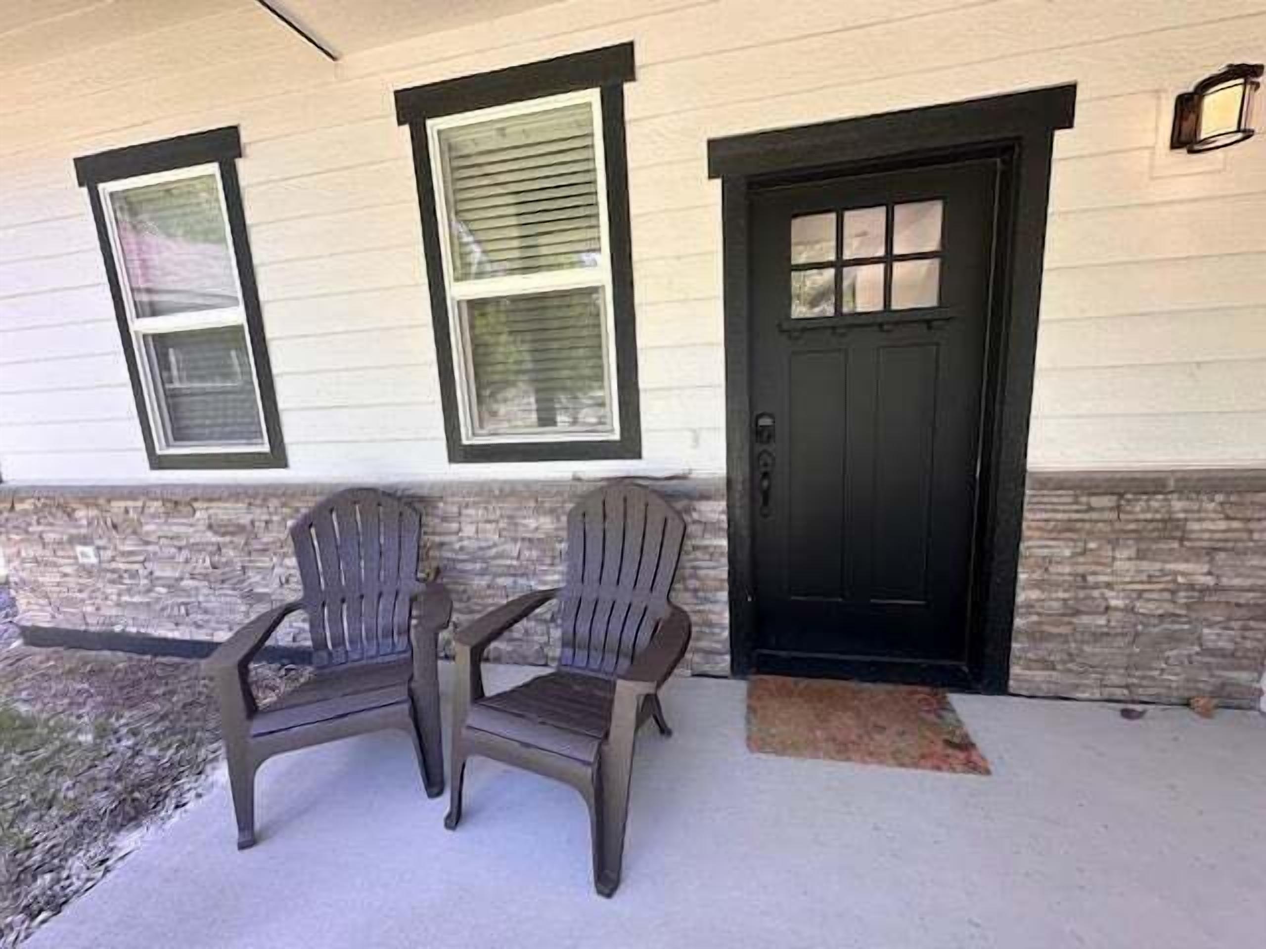 Una casa con porche delantero, dos sillas Adirondack, una puerta negra y un muro de piedra decorativo.