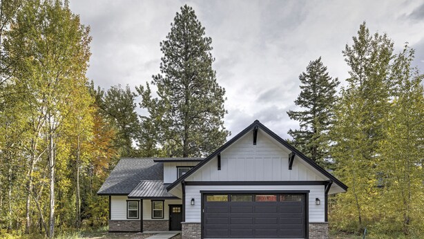 A modern two-story house with a dark garage door, surrounded by tall trees and a cloudy sky. - Brand new incredible Columbia Falls home - Flathead river walking trail - A/C for hot summer days (Columbia Falls)