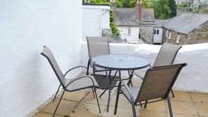 A small outdoor patio with a round metal table and four chairs, surrounded by a white wall and a tiled floor.