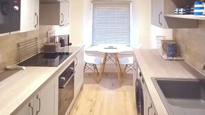 A compact kitchen with a dining table, a microwave, a kettle, and a sink.