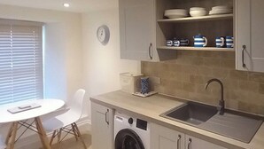 A compact kitchen with a washing machine, a sink, and a dining area with a table and chairs.