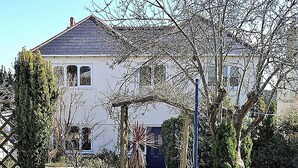Una casa con un vialetto lastricato che conduce all'ingresso, circondata dal verde e con un cielo sereno.