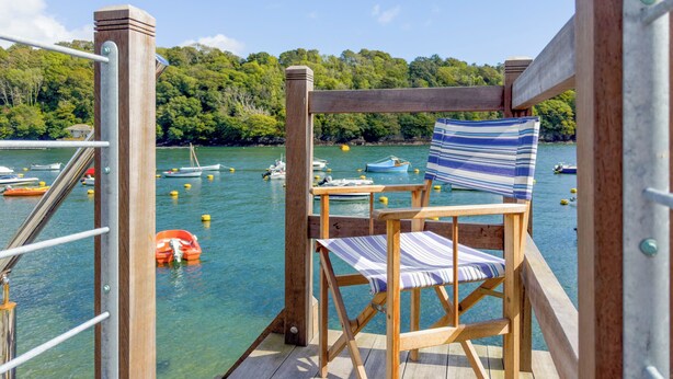 A wooden deck with a striped chair and a view of boats on calm water. - 2 bedroom accommodation in Fowey (Fowey)