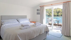 A hotel room with a large bed, a bedside table, a chair, and a view of a body of water with boats. - 2 bedroom accommodation in Fowey (Fowey)