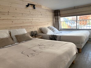 A bedroom with two beds, wooden panel walls, a window with curtains, and a nightstand with a lamp. - APART 2 ALPS, 8 PERS, STATION CENTER, BEAUTIFUL VIEW (LES DEUX ALPES)