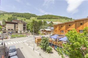 A town with a mix of modern and traditional buildings, a clear road, and a hilly backdrop. - APART 2 ALPS, 8 PERS, STATION CENTER, BEAUTIFUL VIEW (LES DEUX ALPES)