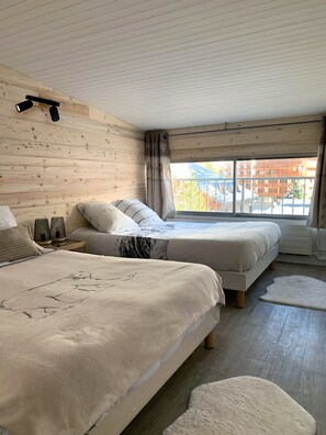 A bedroom with two beds, wooden walls, a large window, and a ceiling light fixture. - APART 2 ALPS, 8 PERS, STATION CENTER, BEAUTIFUL VIEW (LES DEUX ALPES)