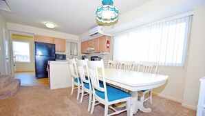 A compact kitchen with a refrigerator, microwave, and stove. There is a dining area with a white table and blue chairs. - Ocean Club 4011-Oceanfront 40th St, Free WiFi, W/D, AC (Ocean City)
