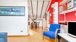 Une pièce avec un plancher en bois, une chaise bleue, un téléviseur à écran plat et un mur rouge orné d’étagères.